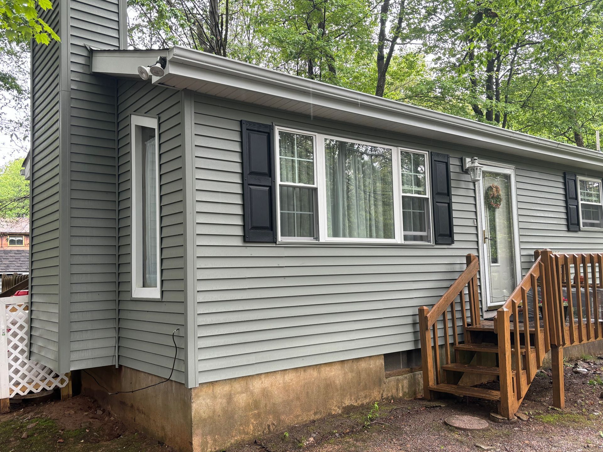 Gray single-story house with black shutters, a prominent chimney, and wooden steps leading to a side entrance.