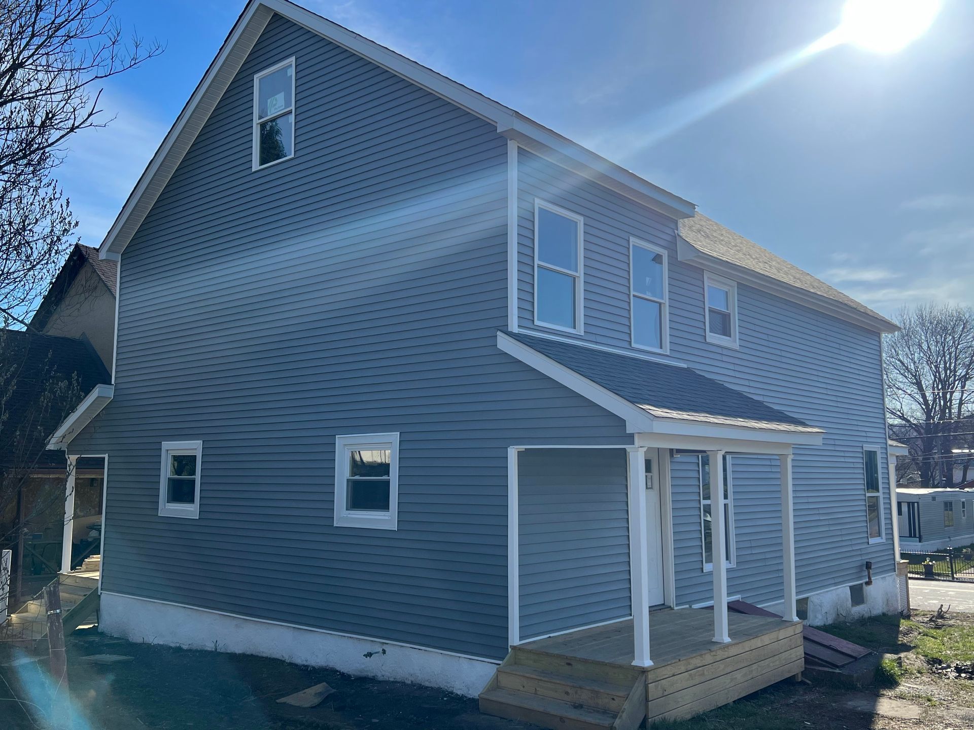 A side and front view of a two-story house with light blue siding, a white front porch, and a white foundation.