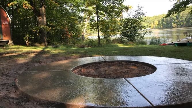 A fire pit is sitting in the middle of a lush green field next to a lake.
