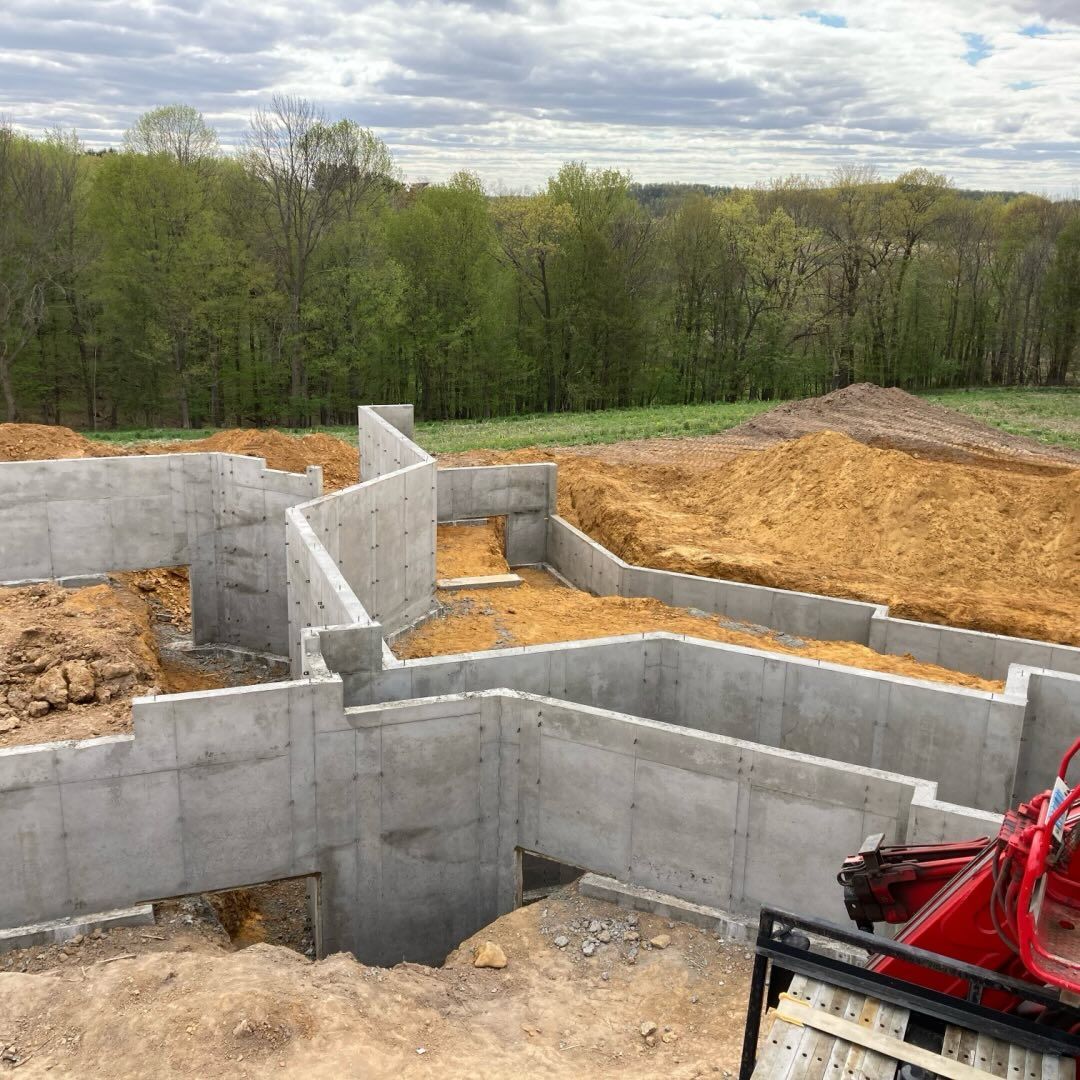 Concrete foundation for a building under construction, with surrounding earth and trees in the background.