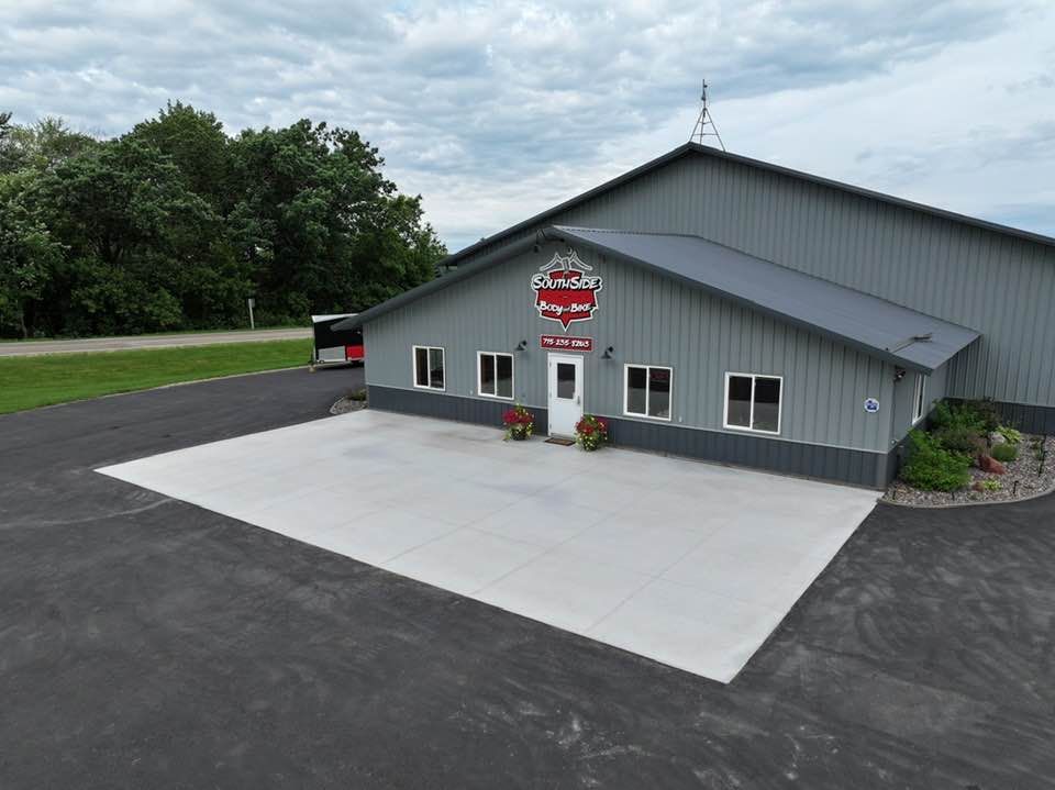 Gray commercial building with large concrete patio, trees, and cloudy sky.