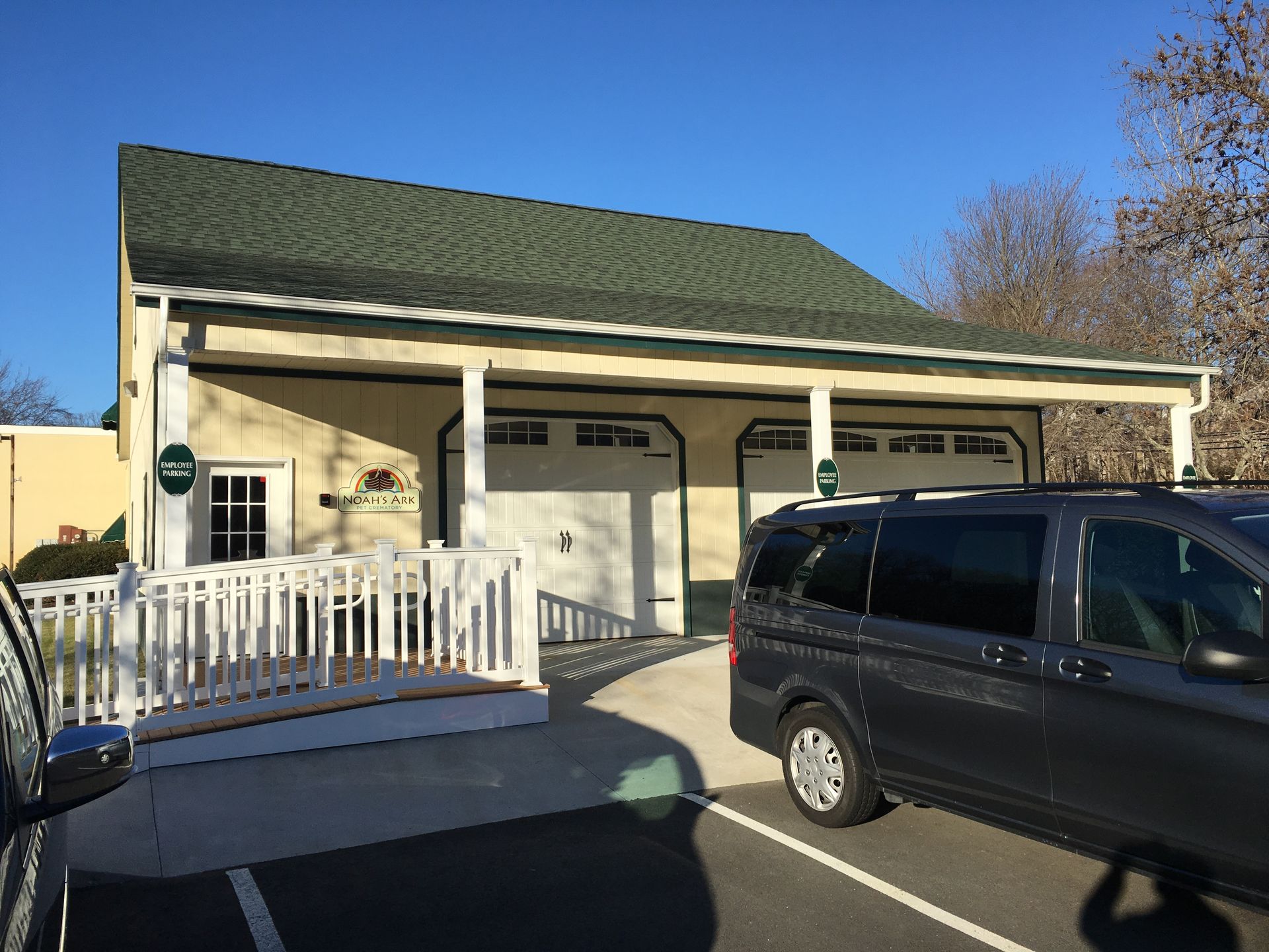Driveway view of a beige house with green roof and porch, with a black SUV parked in front.