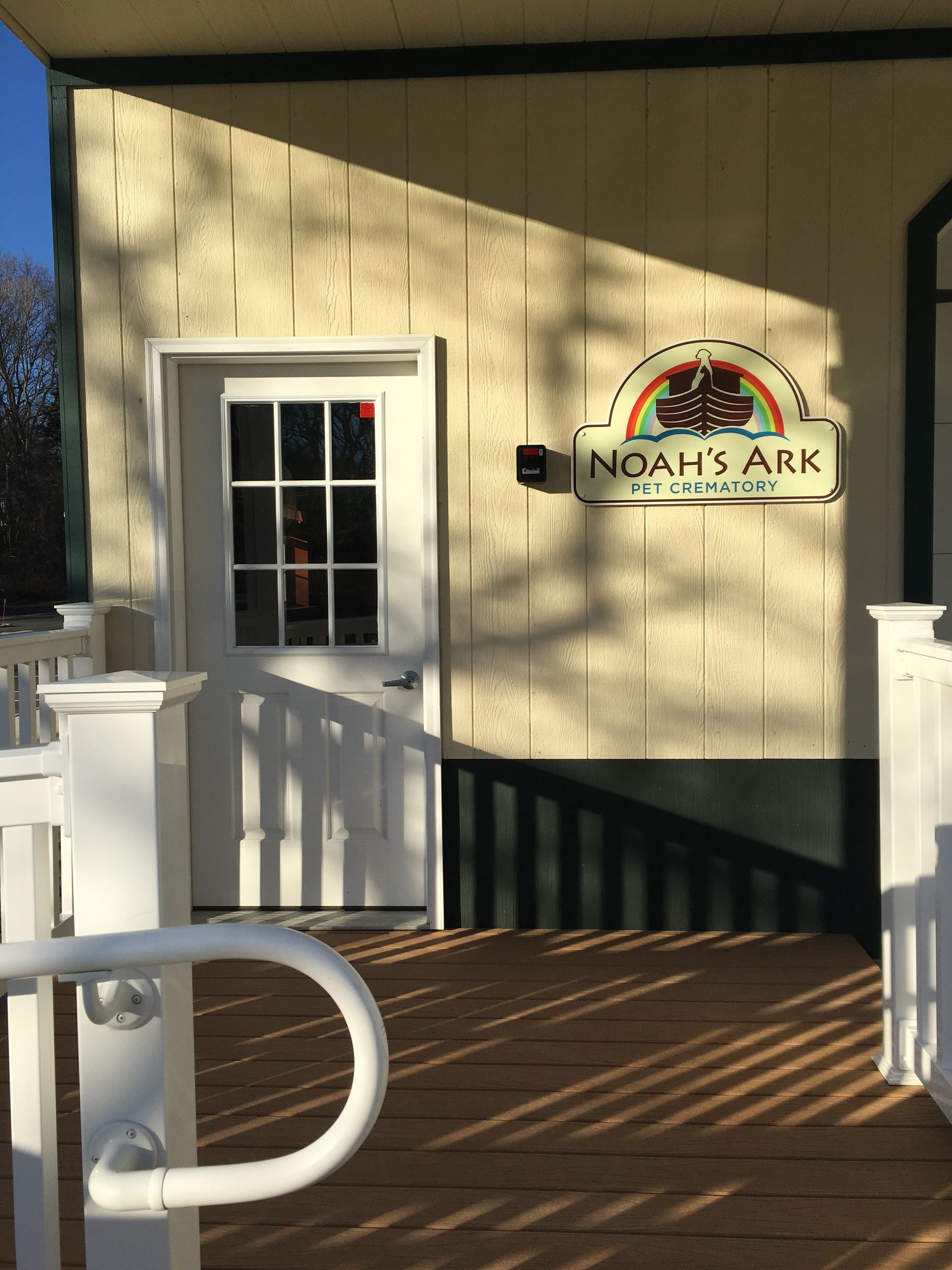Entrance porch with a Noah’s Ark sign on a beige building, featuring white railings and a door.