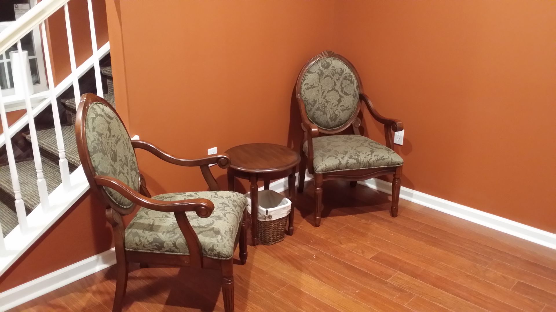 Two upholstered chairs and a small wooden table in a corner with orange walls and hardwood floor