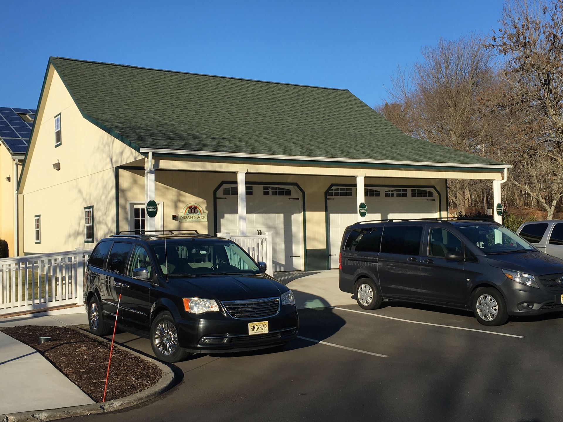 Black minivan and van parked outside a beige house with a covered porch on a sunny day