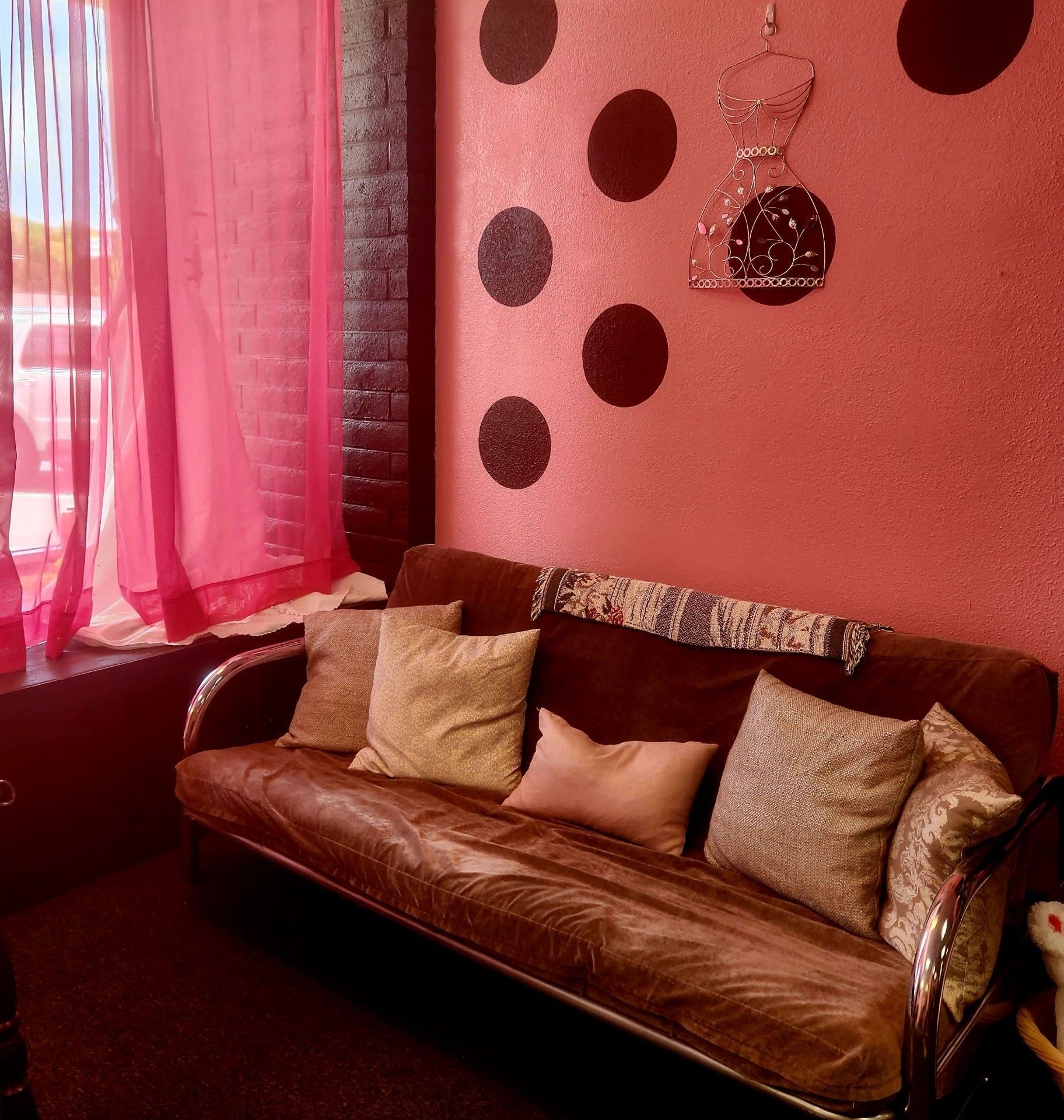 A brown couch in front of a pink wall with polka dots