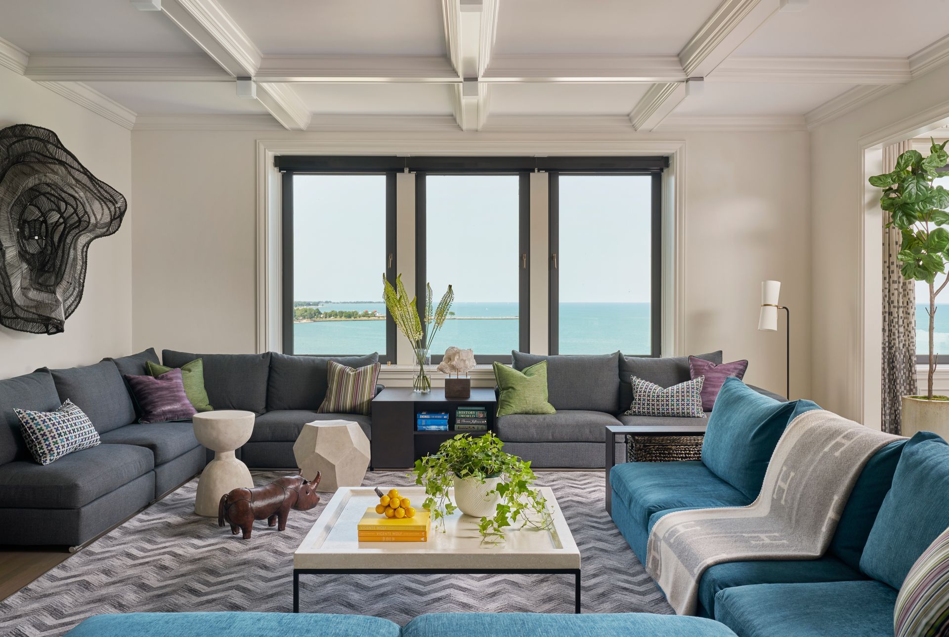 A living room with blue couches and a coffee table with a view of the ocean.