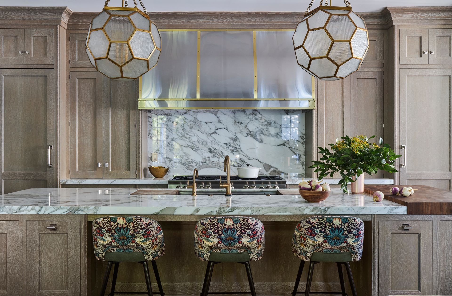 A kitchen with a large island, stools, a stove, and a sink.