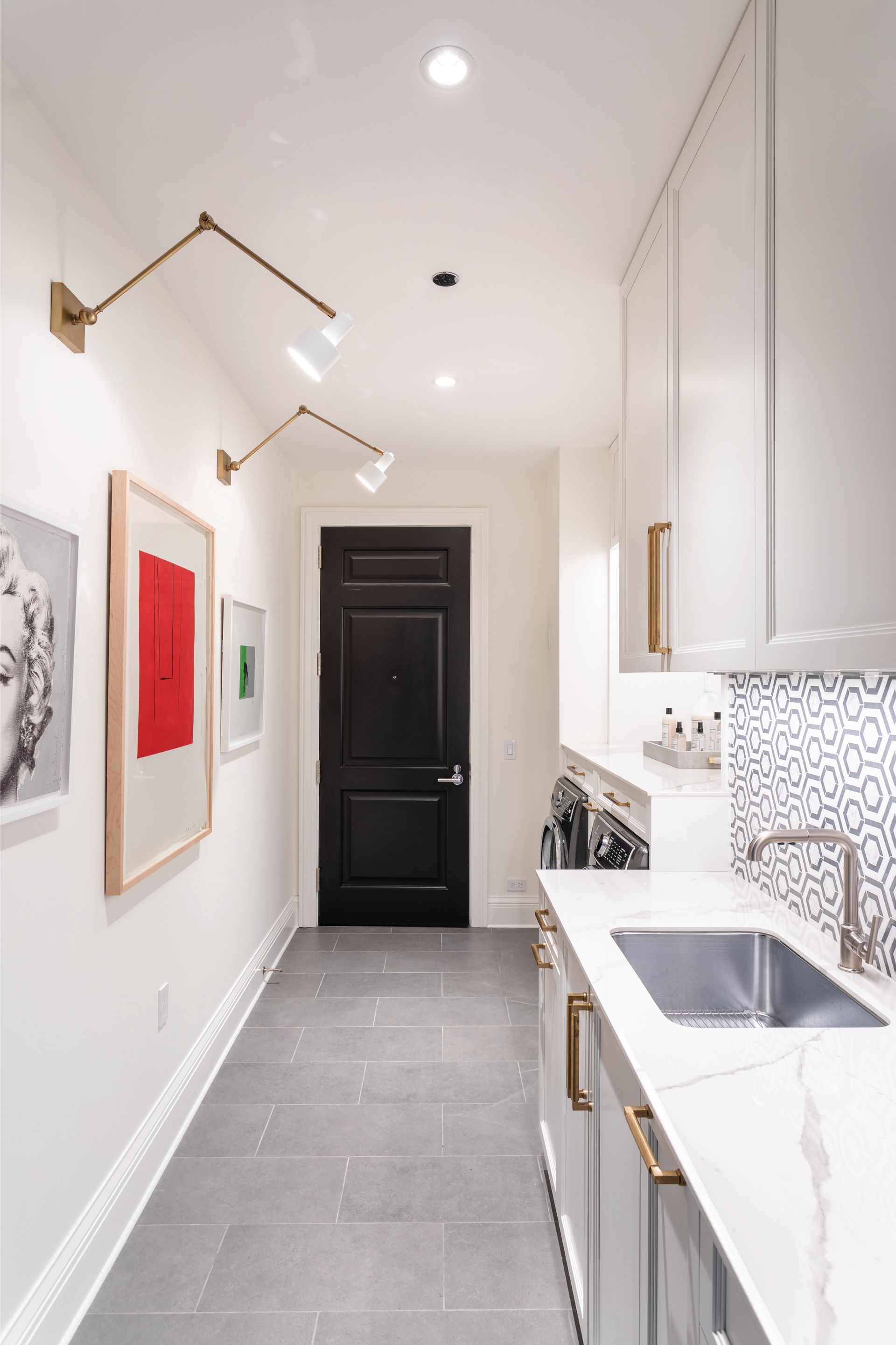 A long hallway leading to a kitchen with white cabinets and a sink.