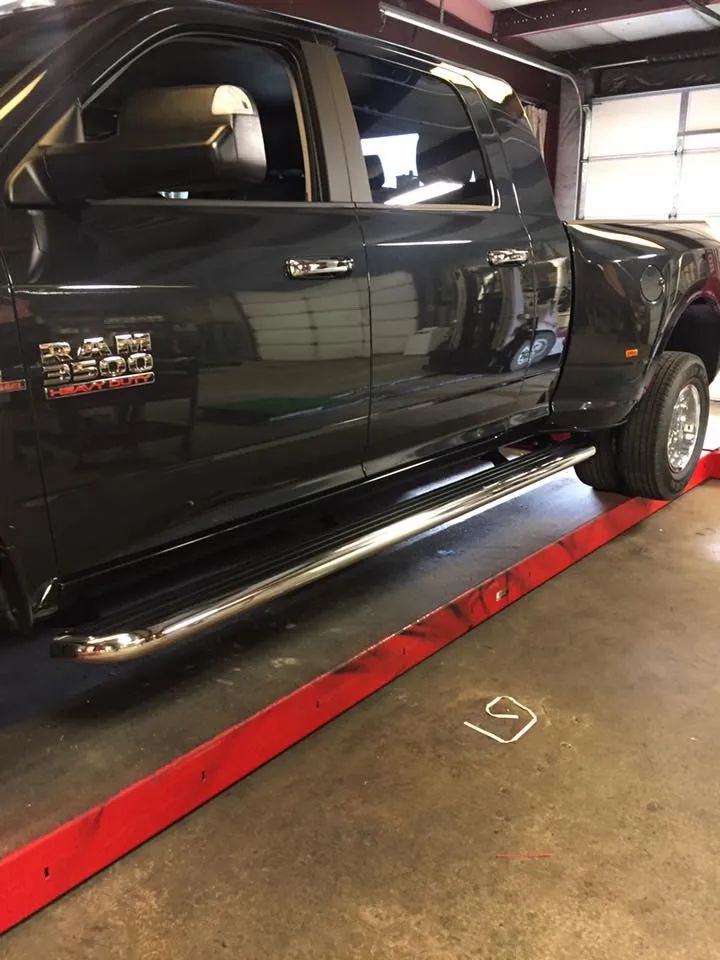 Black Ram 3500 dually truck with chrome running boards on a red lift inside a garage.