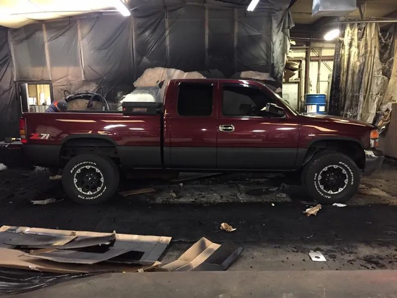 Red and gray pickup truck in a cluttered garage, possibly under repair.