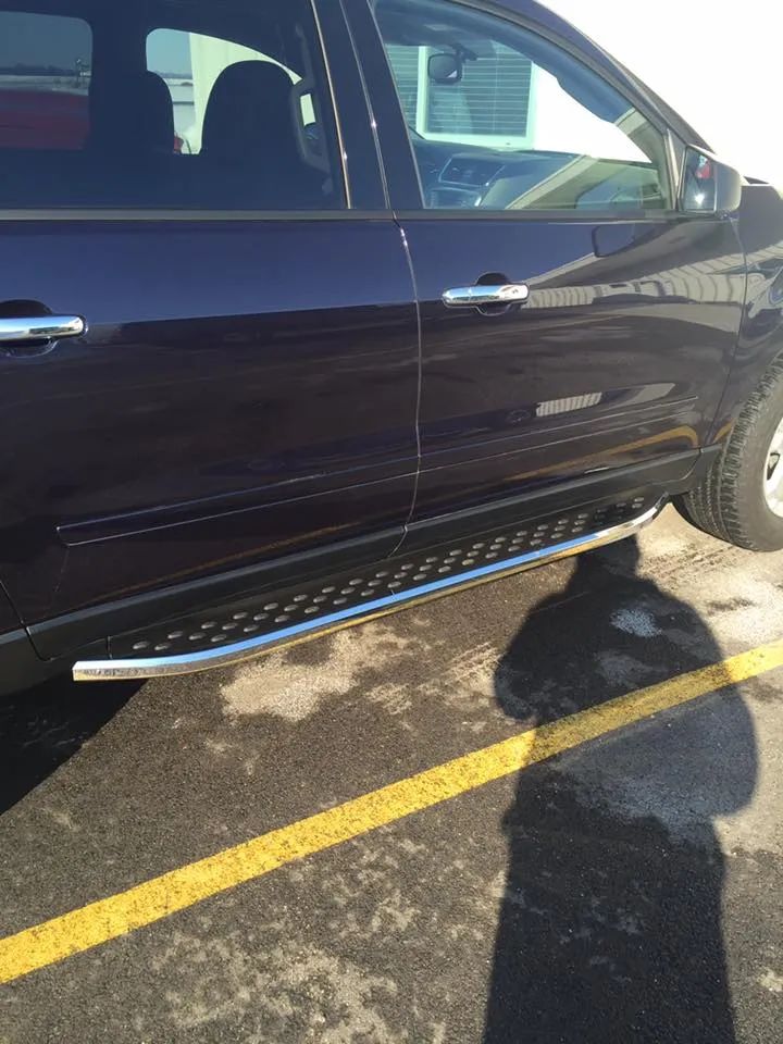 Dark blue SUV with running boards parked on asphalt next to a yellow line; shadow of a person.