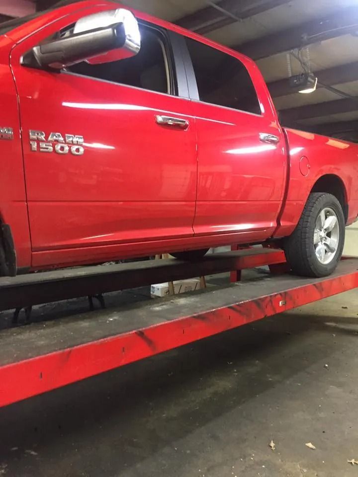 Red Ram 1500 truck on a red lift inside a garage. The truck's side and silver mirror are visible.