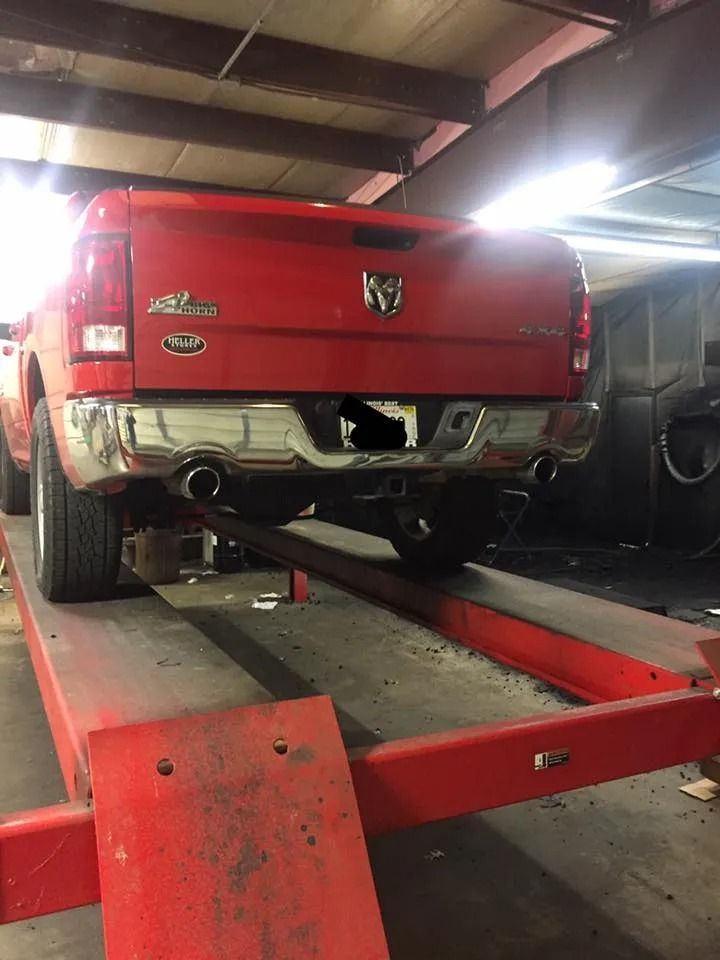 Red Dodge Ram pickup truck on a red automotive lift, viewed from the rear, inside a garage.