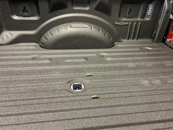 Truck bed with spray-in bedliner, recessed hitch, and wheel well cover. Textured, black surface.