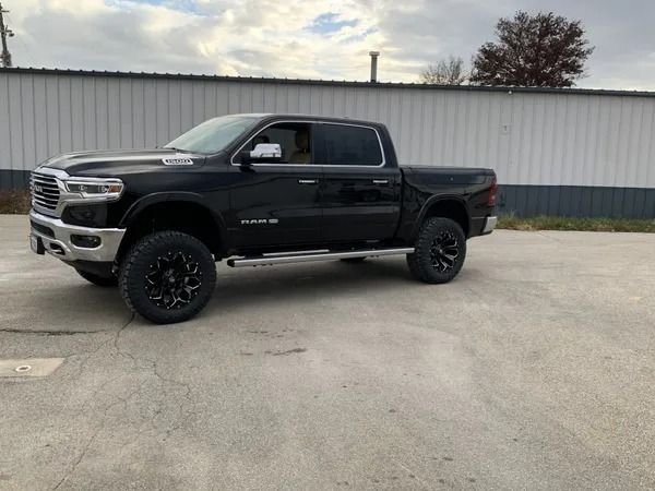 Black Ram truck, lifted with black wheels, parked in front of a white building.