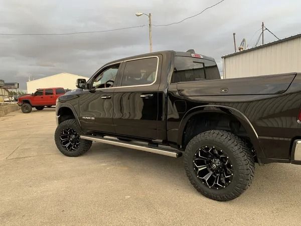 Black lifted Ram pickup truck with black and silver wheels, parked next to a building on a cloudy day.
