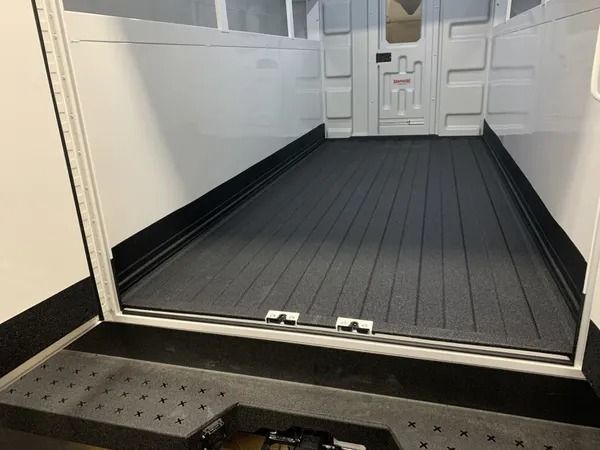 Interior of a white utility van with a black grooved floor. The door is open, showing a loading area.