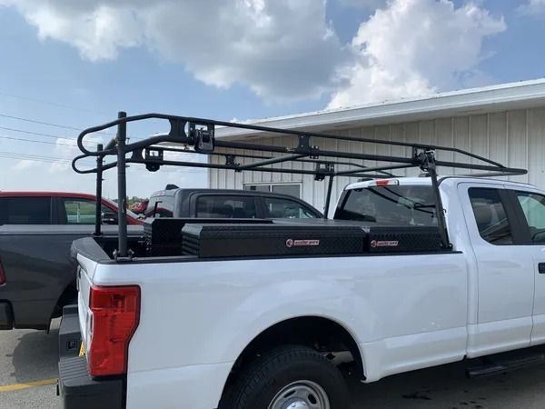 White pickup truck with black rack and toolboxes, parked outside on a cloudy day.
