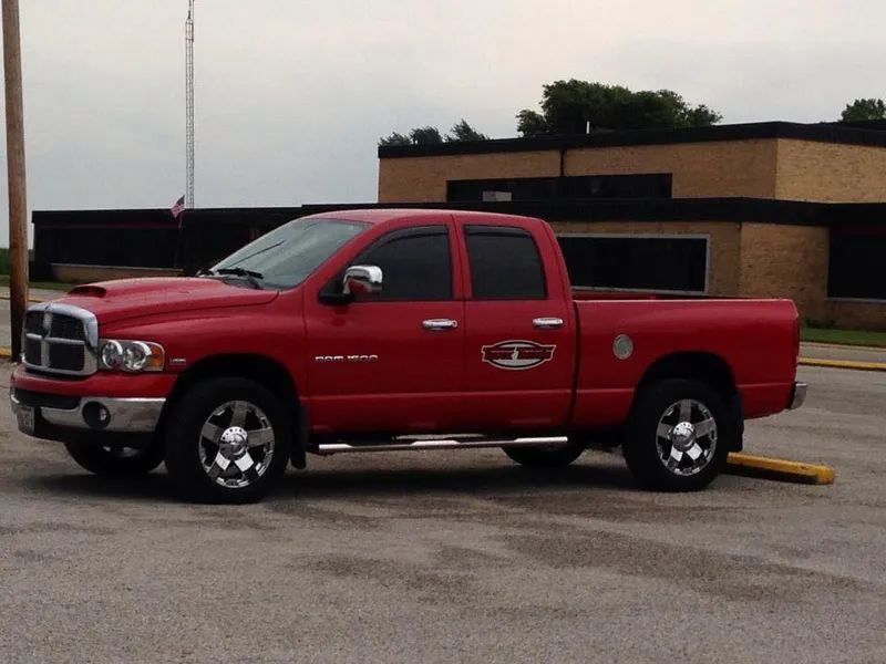 Red Dodge Ram pickup truck parked in a parking lot. It has chrome wheels and running boards.