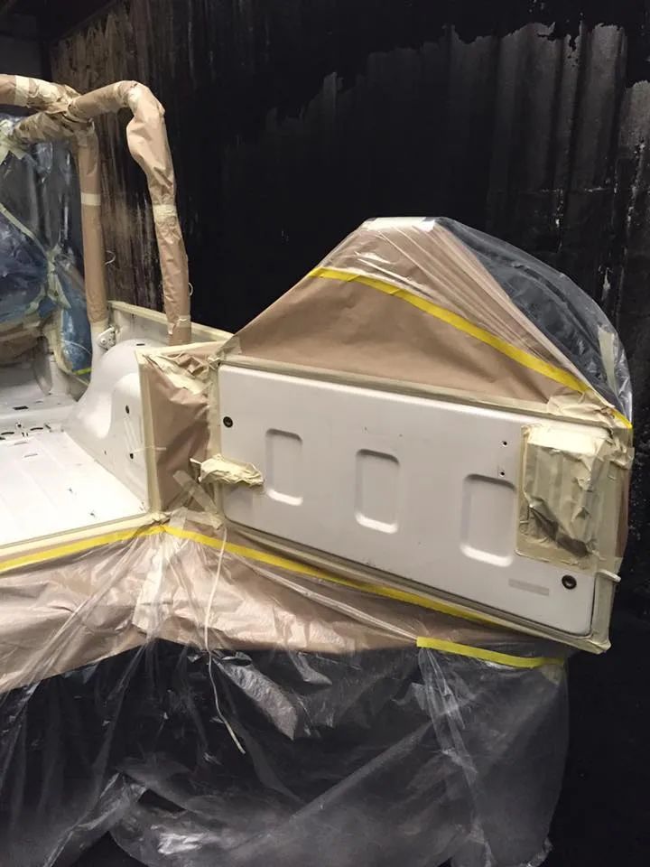 A white vehicle body section, masked with paper and plastic, ready for paint in a dark setting.