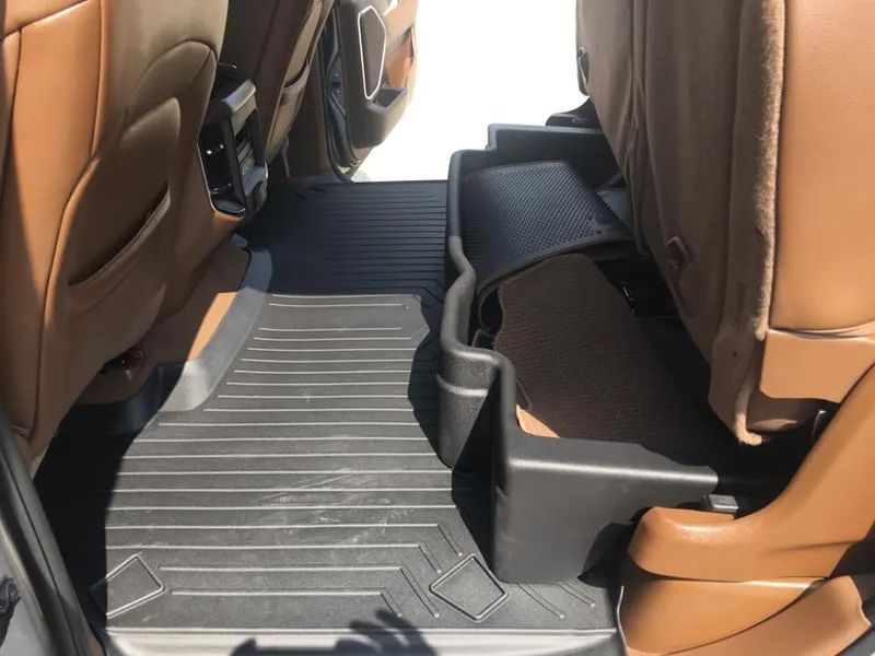 Interior of a vehicle, showing black floor mats in the back seat area between tan seats.