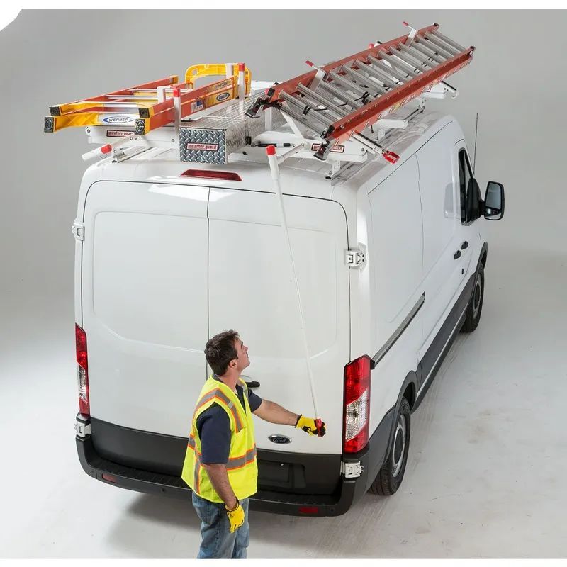 Person in safety vest opening the back of a white van with ladders mounted on the roof.