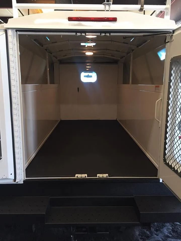 Interior of an empty, white trailer with a dark floor and open back doors.