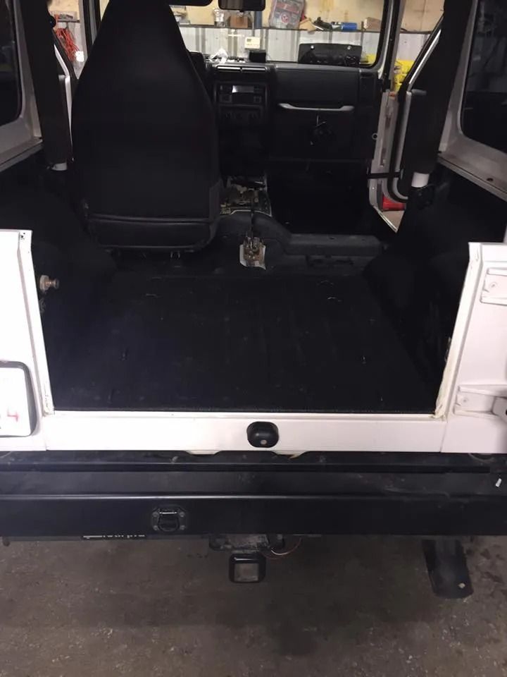 Interior of a white Jeep. Black interior, with rear cargo area visible. Black bumper with trailer hitch.