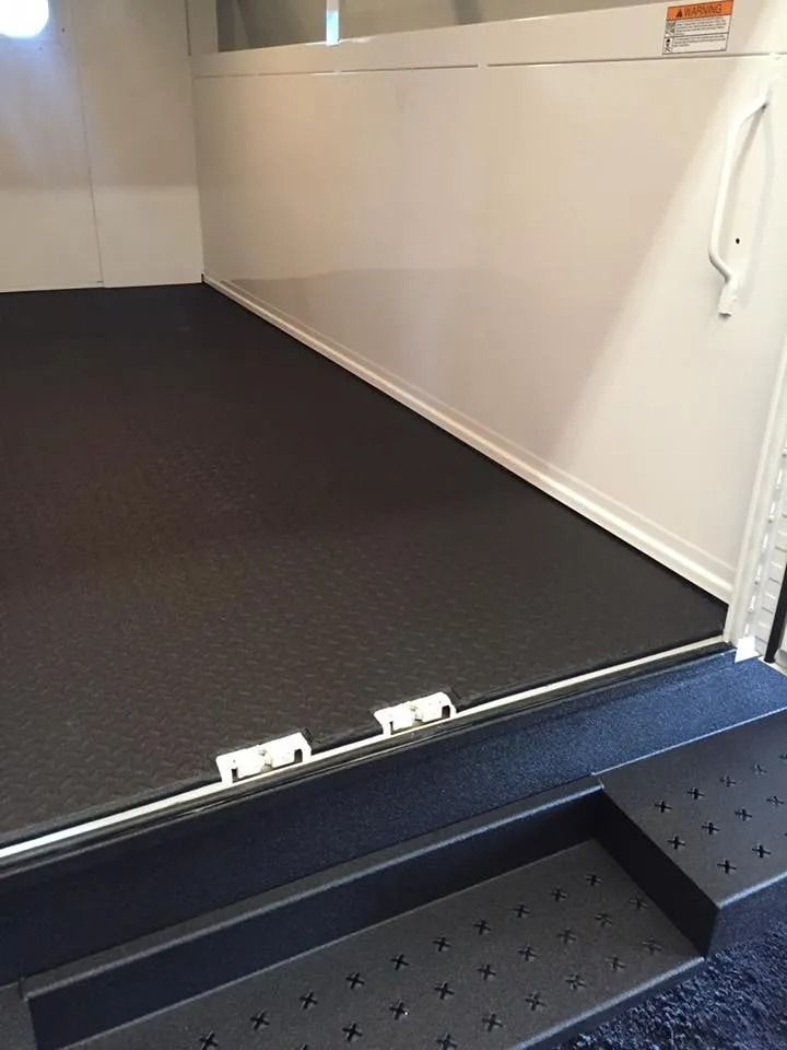 Interior of a horse trailer with black rubber flooring, white walls, and a ramp entrance.