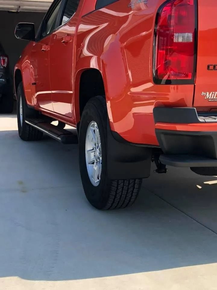 Orange pickup truck, rear quarter view, with black mud flaps and chrome wheel.
