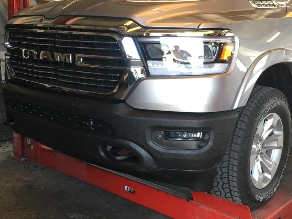 Silver Ram truck front end, black bumper, on a lift. Chrome grill and headlight detail visible.