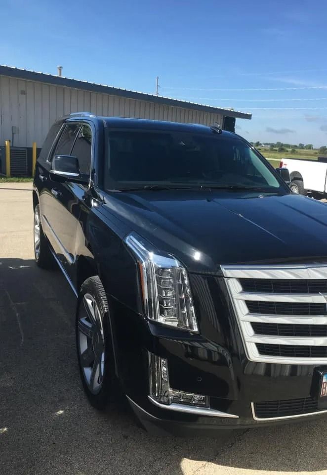 Black Cadillac Escalade SUV parked in front of a building on a sunny day.