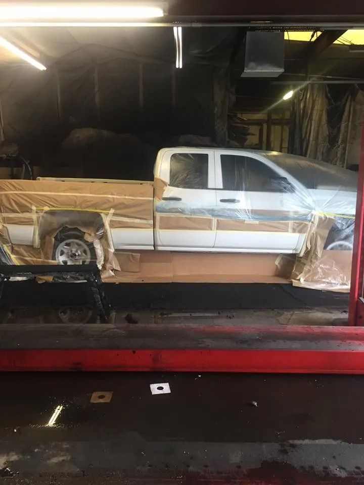 White pickup truck in a repair shop, wrapped in cardboard and plastic.