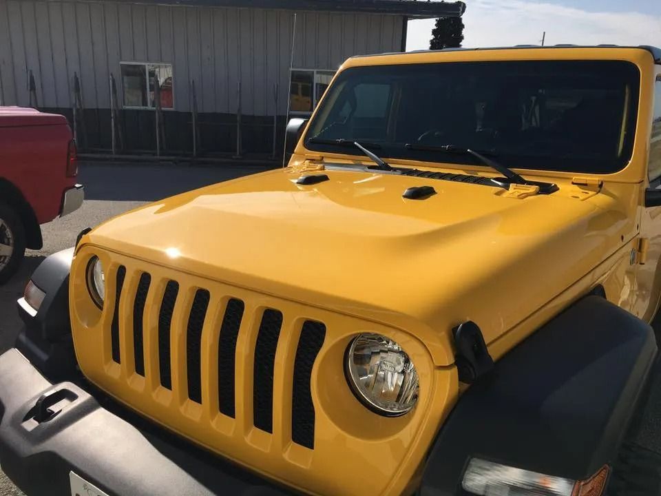 Yellow Jeep Wrangler, front view, black grill, sunny day.