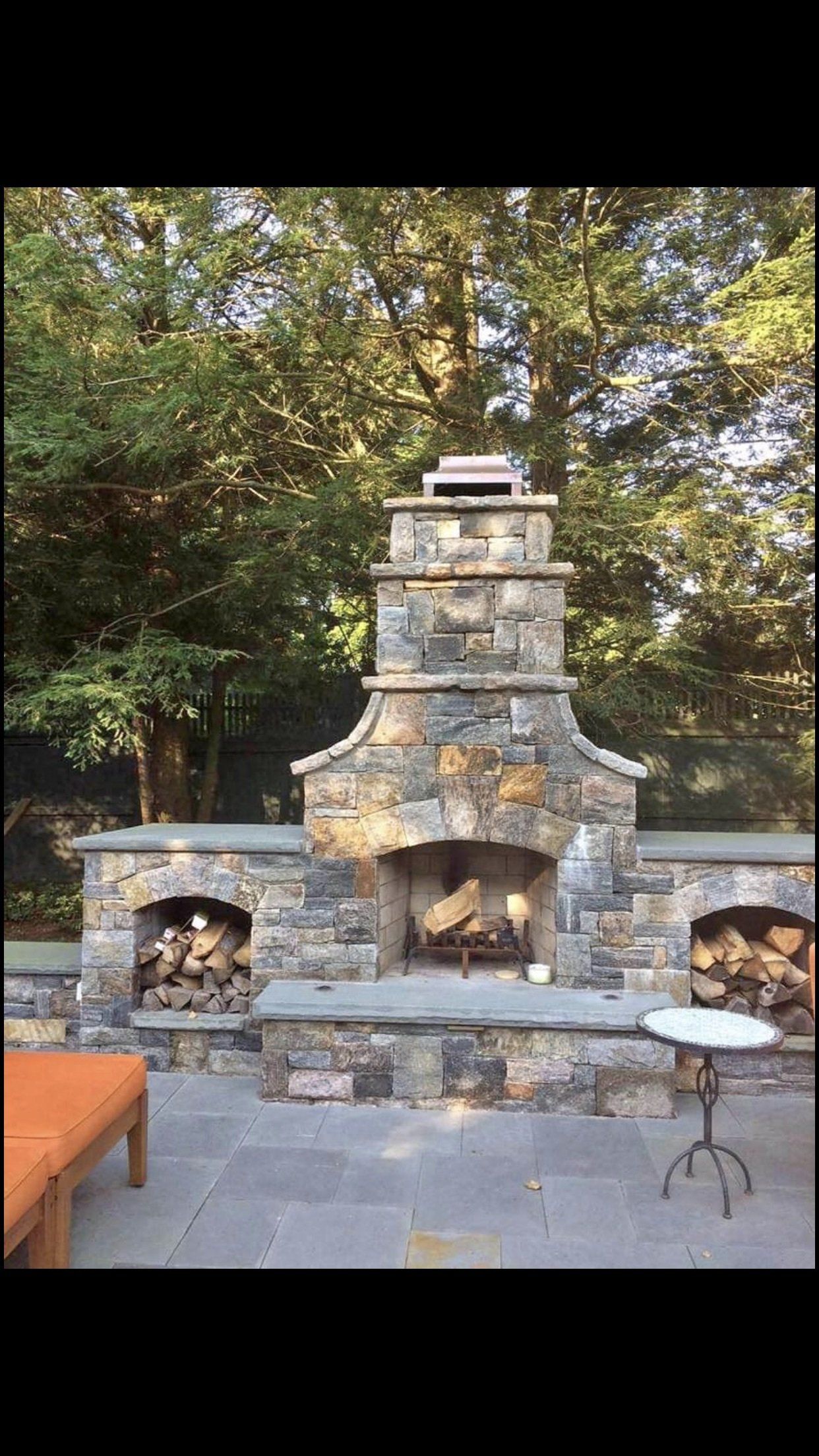A stone fireplace is sitting on top of a patio next to a table.