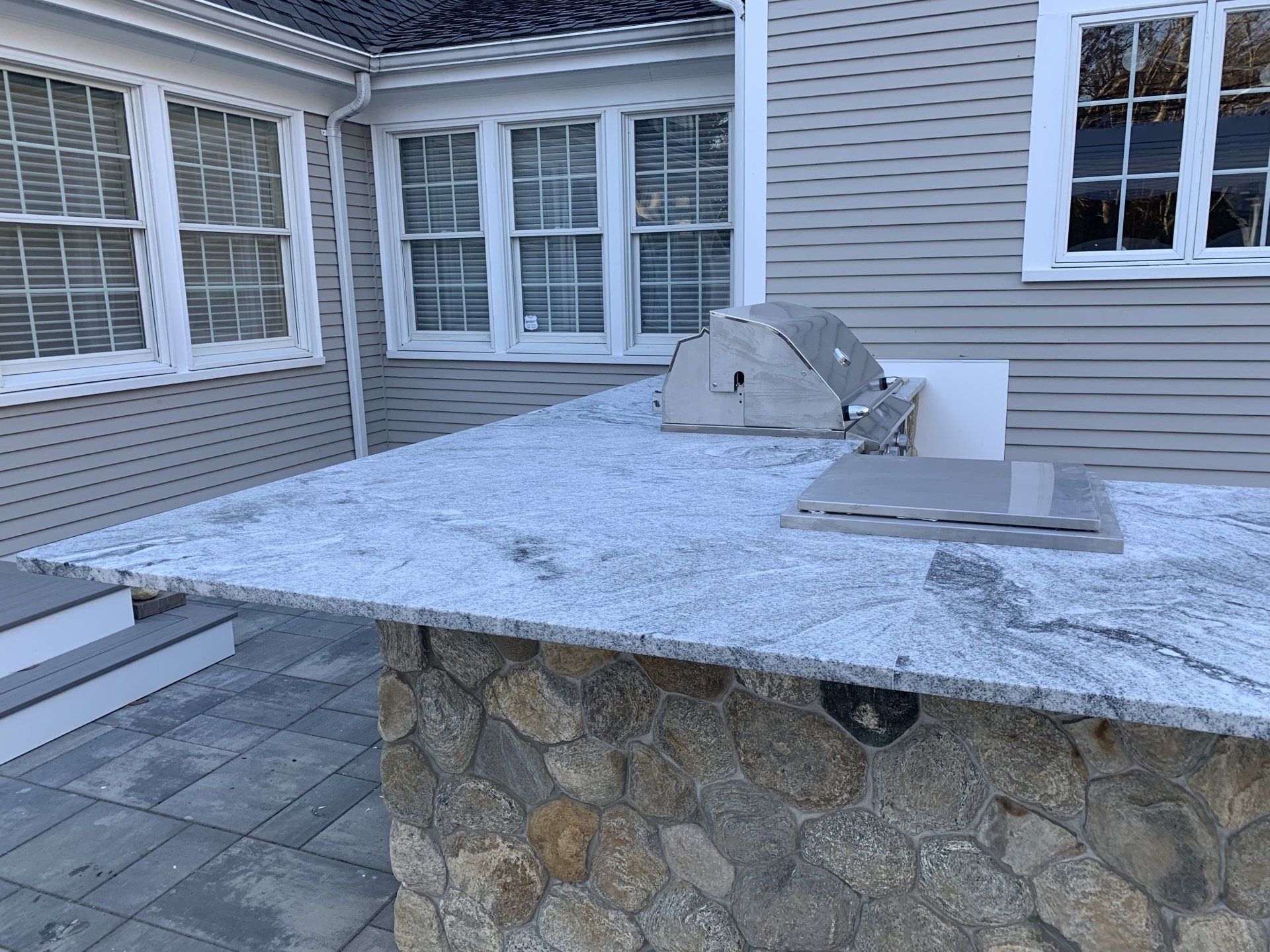 A grill is sitting on top of a granite counter in front of a house