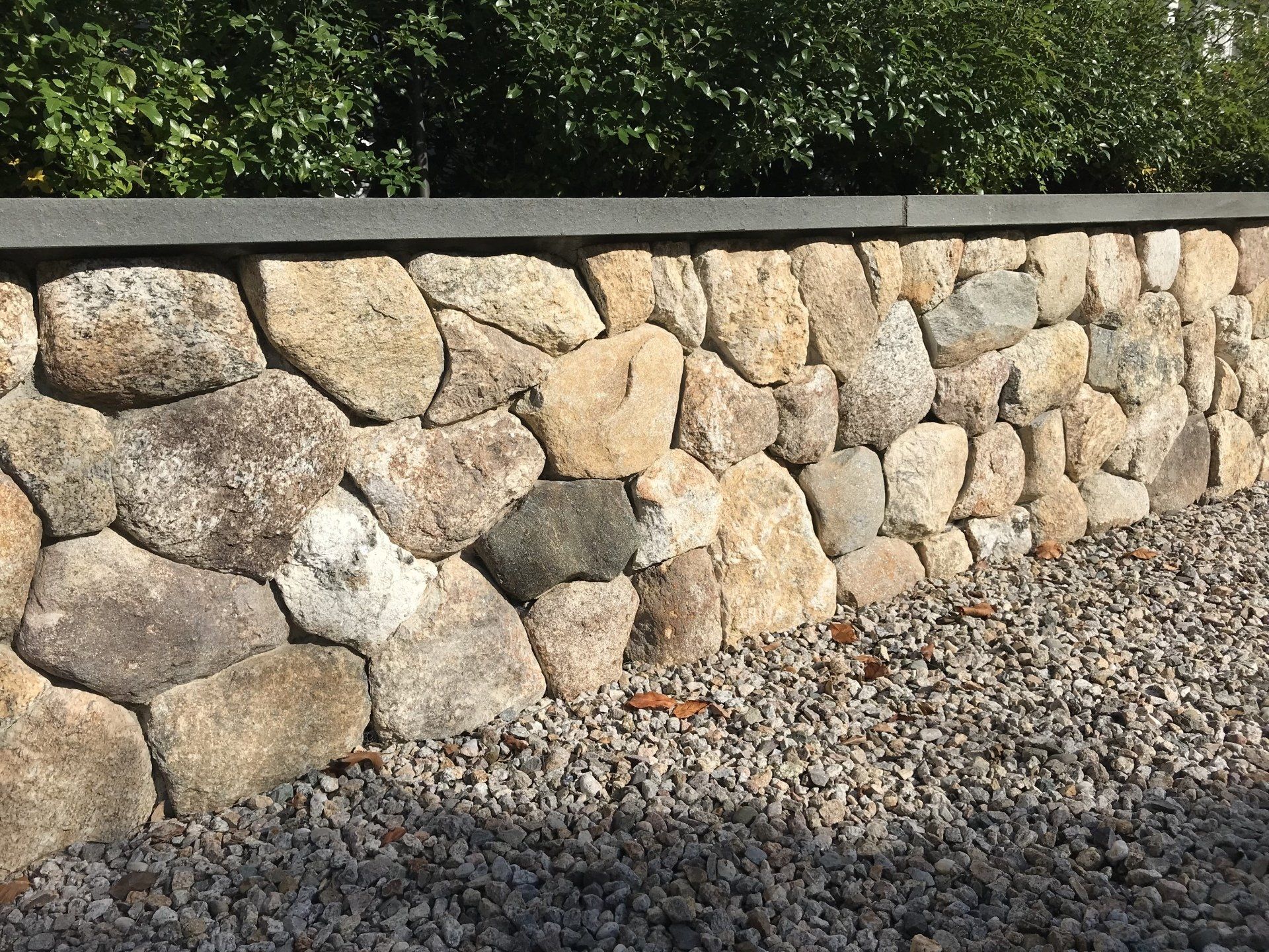 A stone wall is surrounded by gravel and trees