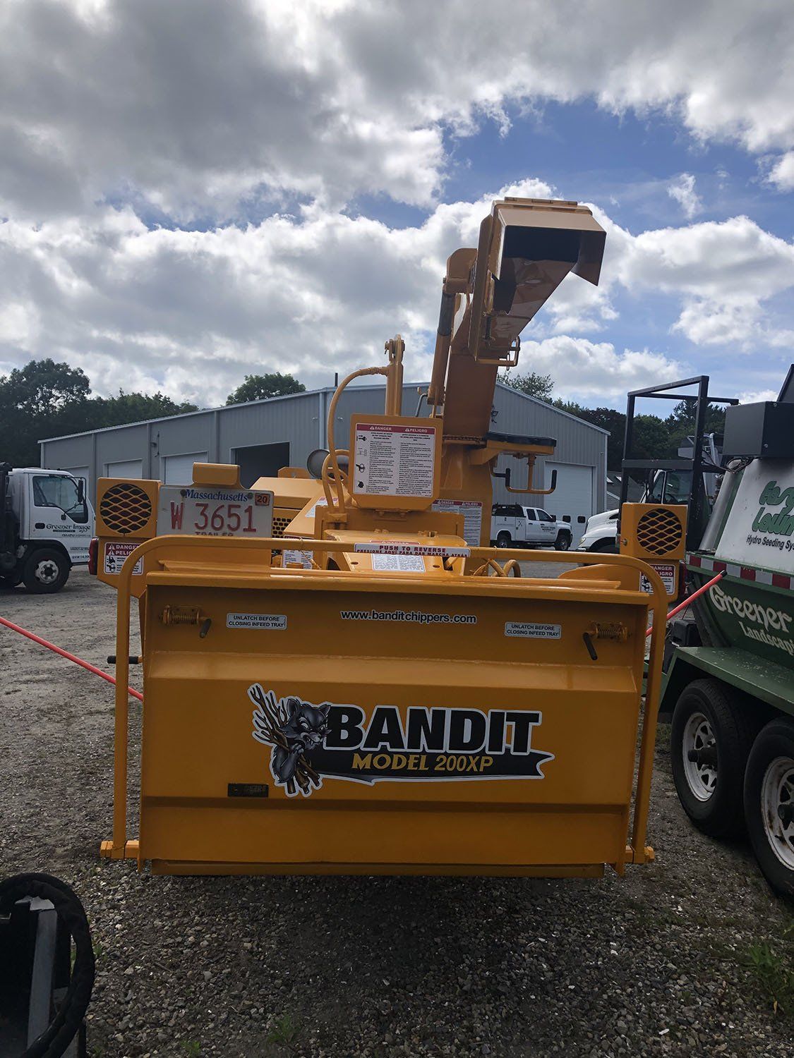 A yellow bandit snow blower is parked in a gravel lot.