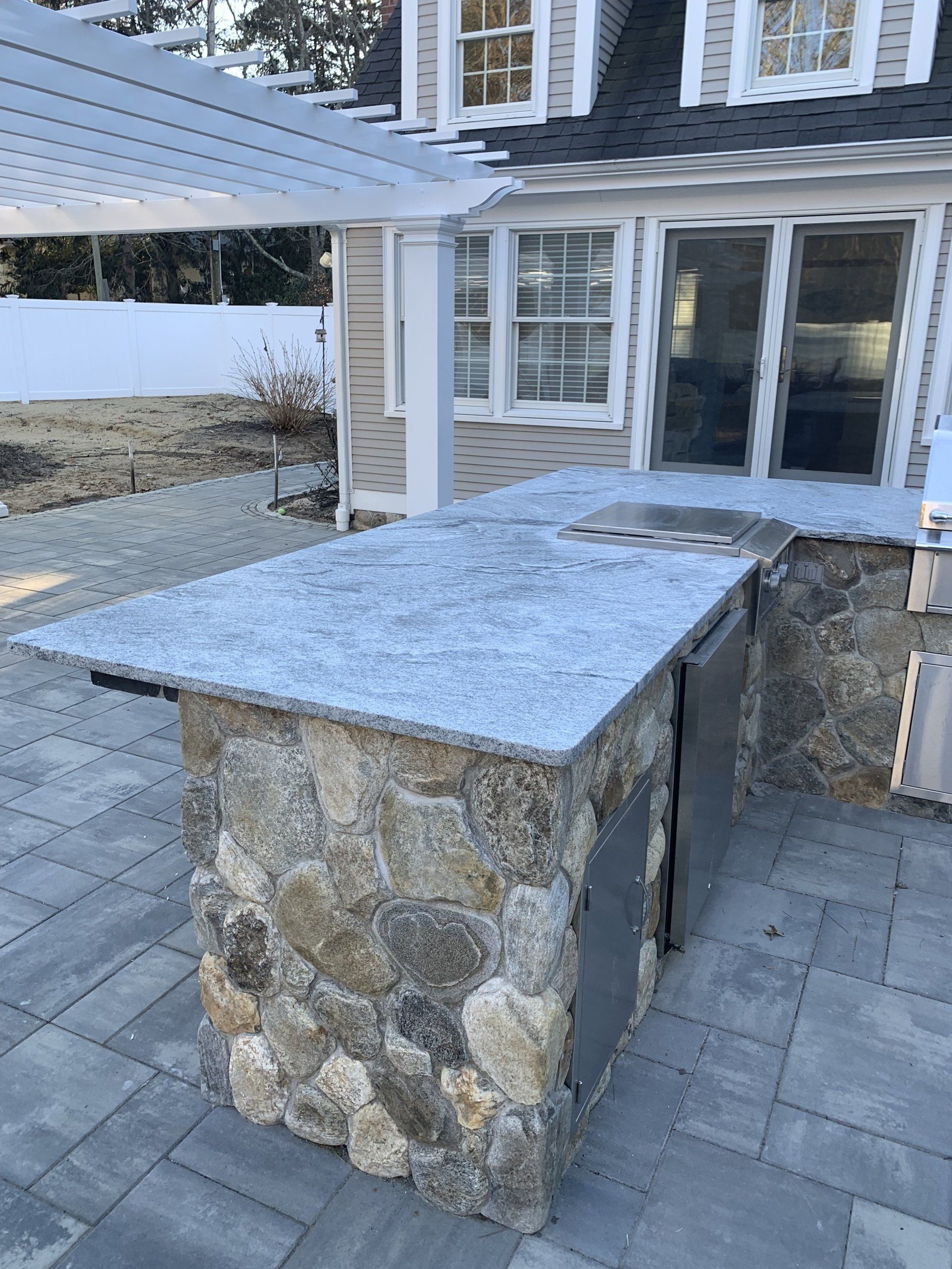 A stone island with a granite counter top is sitting on a patio in front of a house