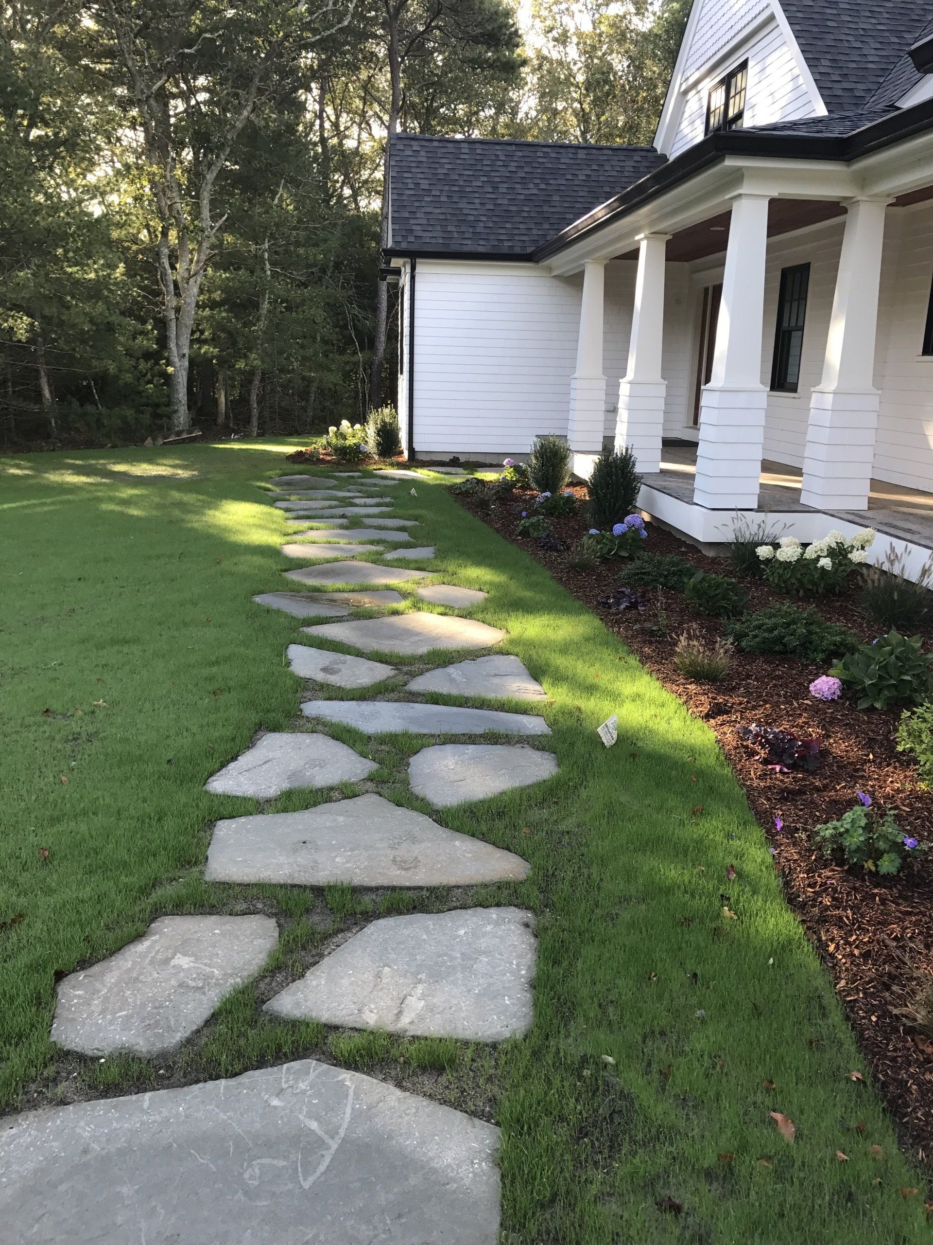 A stone walkway leading to a white house with a porch