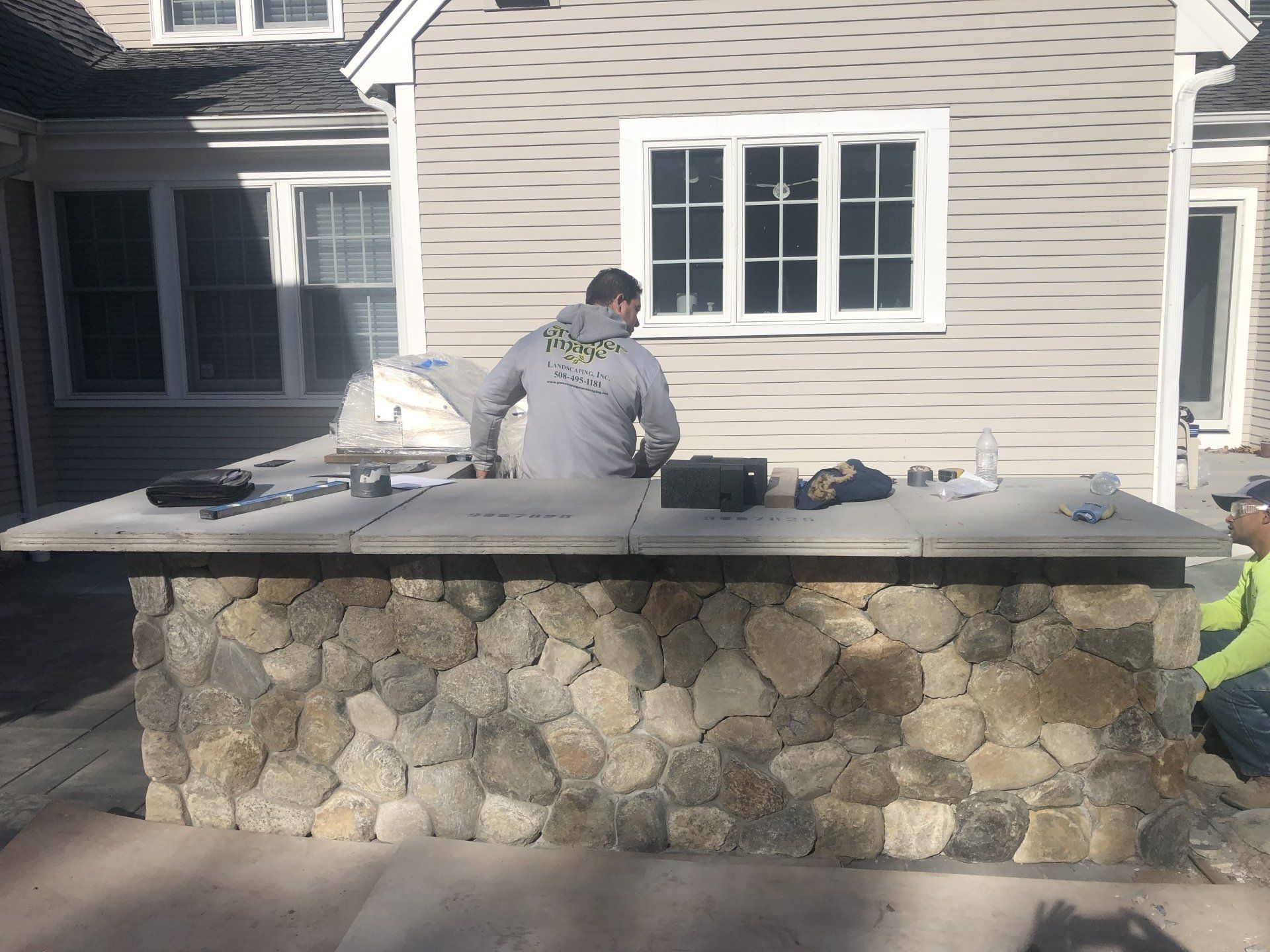 A man is standing behind a stone counter in front of a house