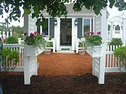 A white house with a white fence and flowers in front of it