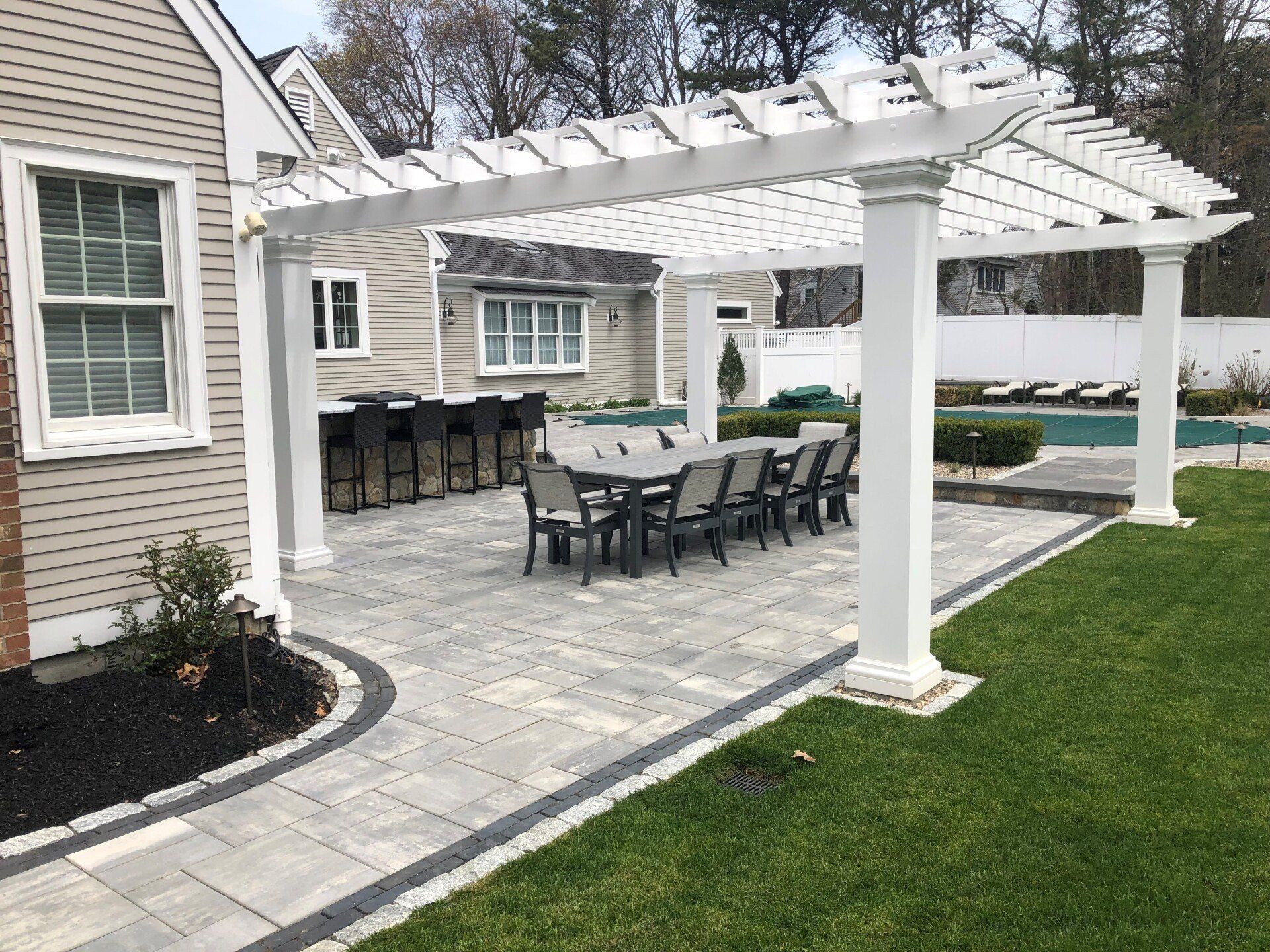A patio with a table and chairs under a pergola in front of a house