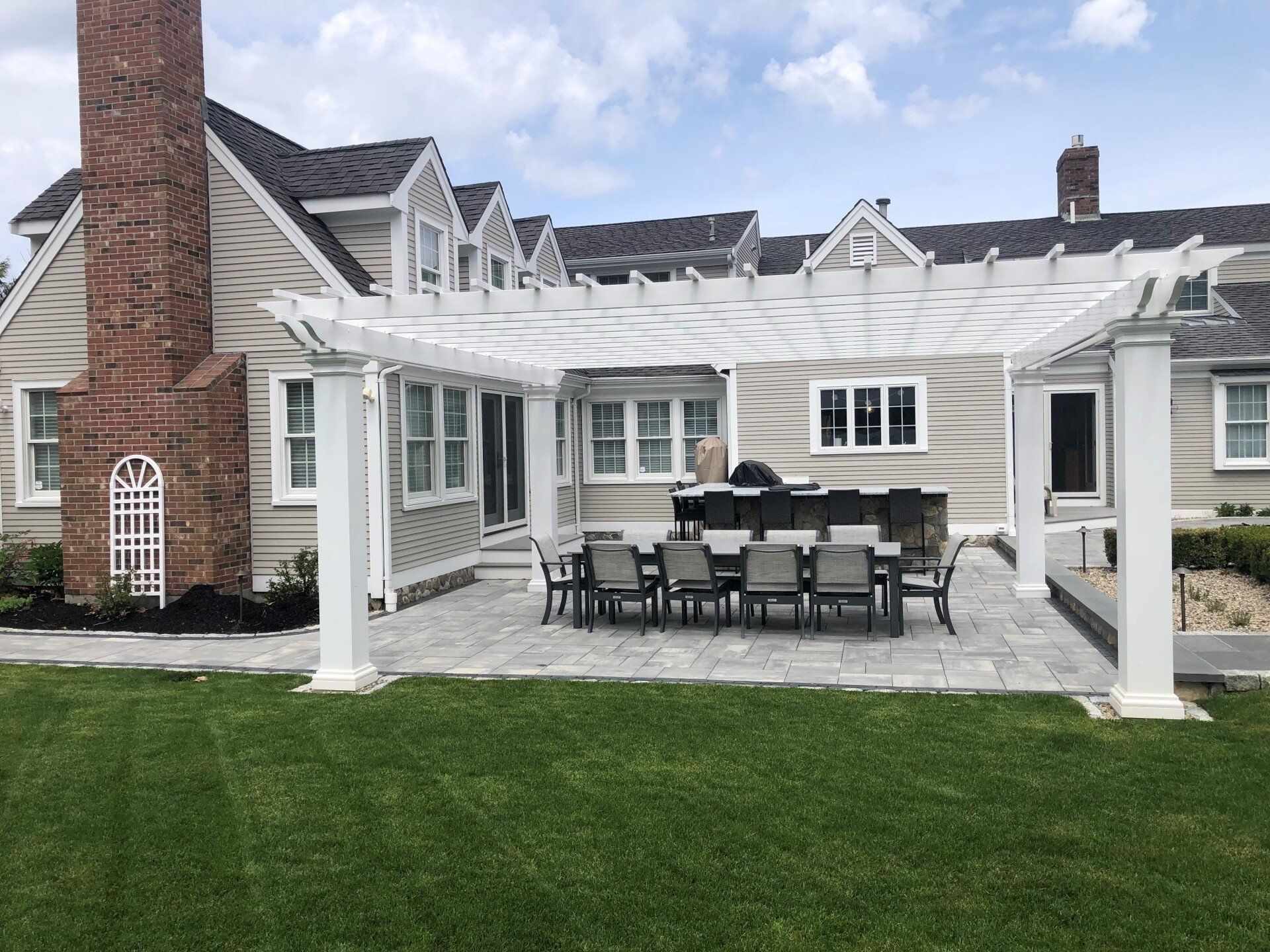 A large house with a pergola over a patio with a table and chairs