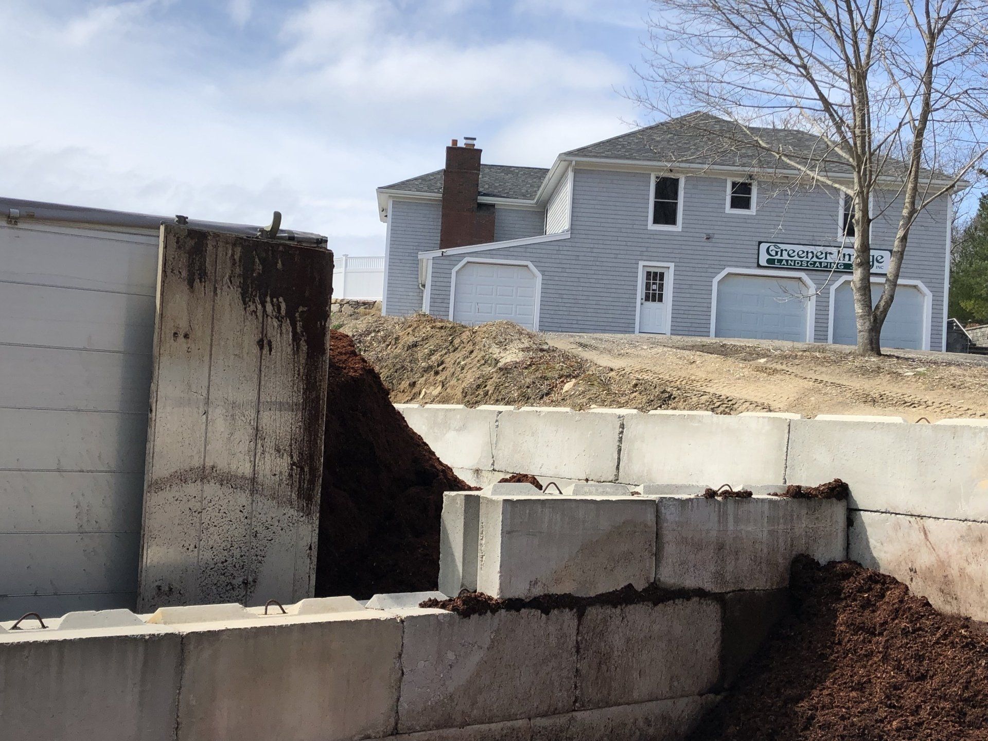 A truck delivers mulch near a gray building, with mounds of fresh mulch piled up.