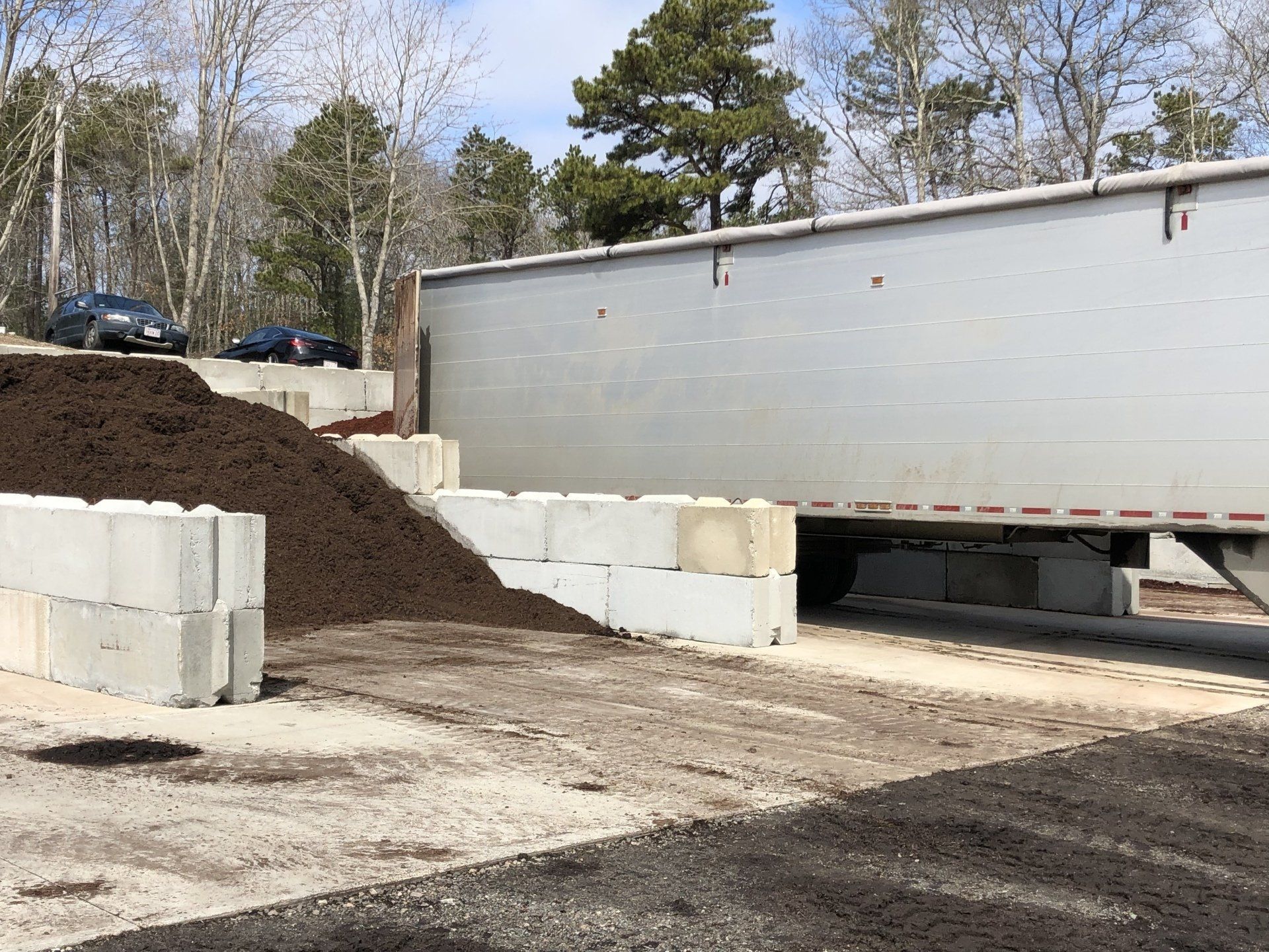 A truck unloads mulch near concrete barriers.