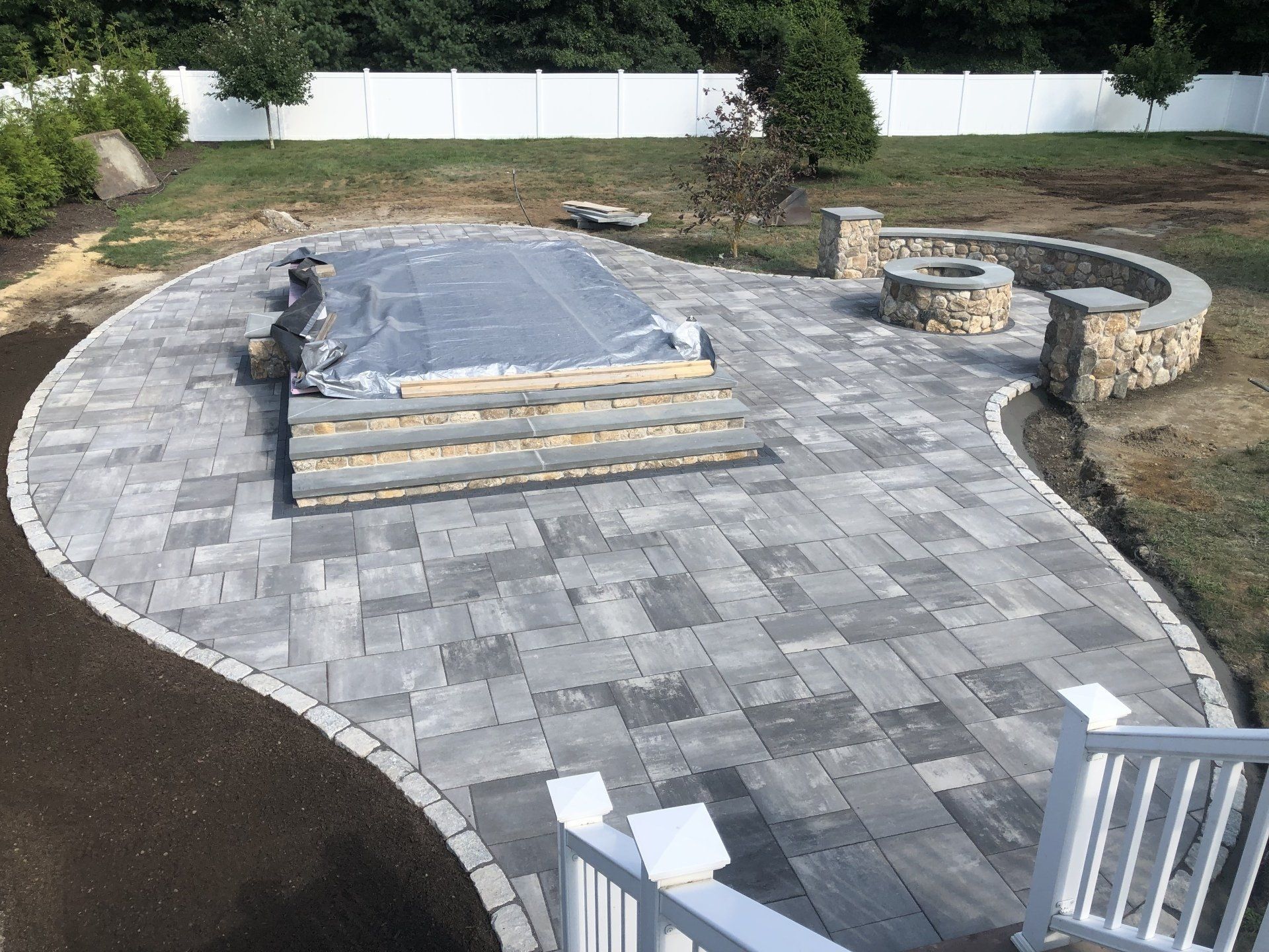 A patio is being built in a backyard with a fire pit.