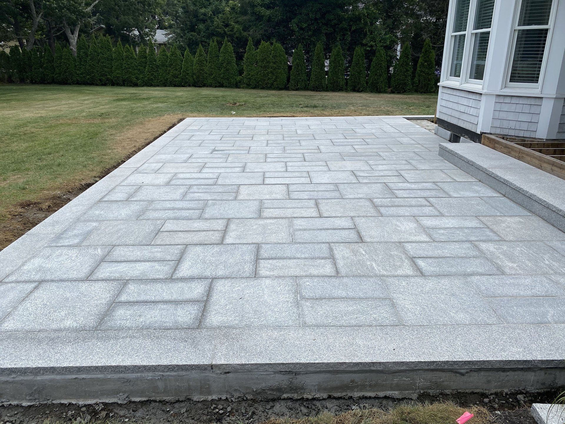 A brick patio is being built in the backyard of a house.