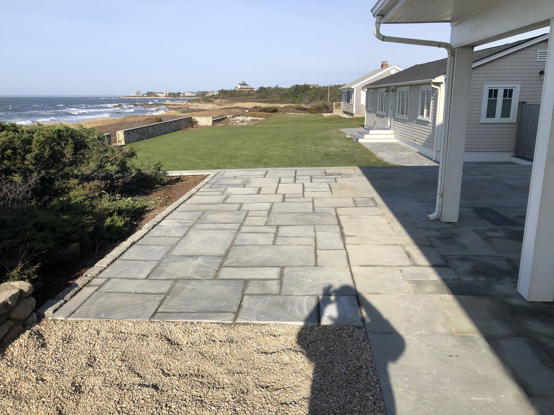 A patio with a view of the ocean and a house in the background.